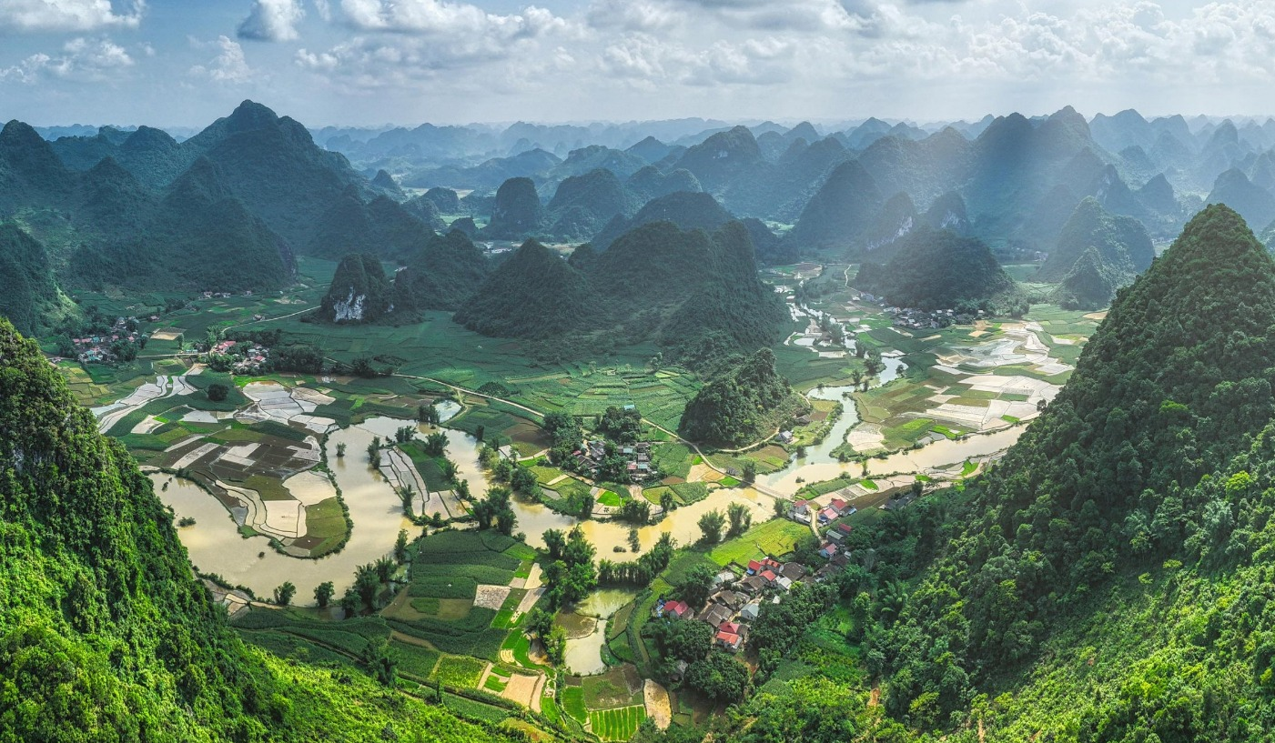 Aerial view of green mountains, fields and winding waterways beneath a cloudy sky